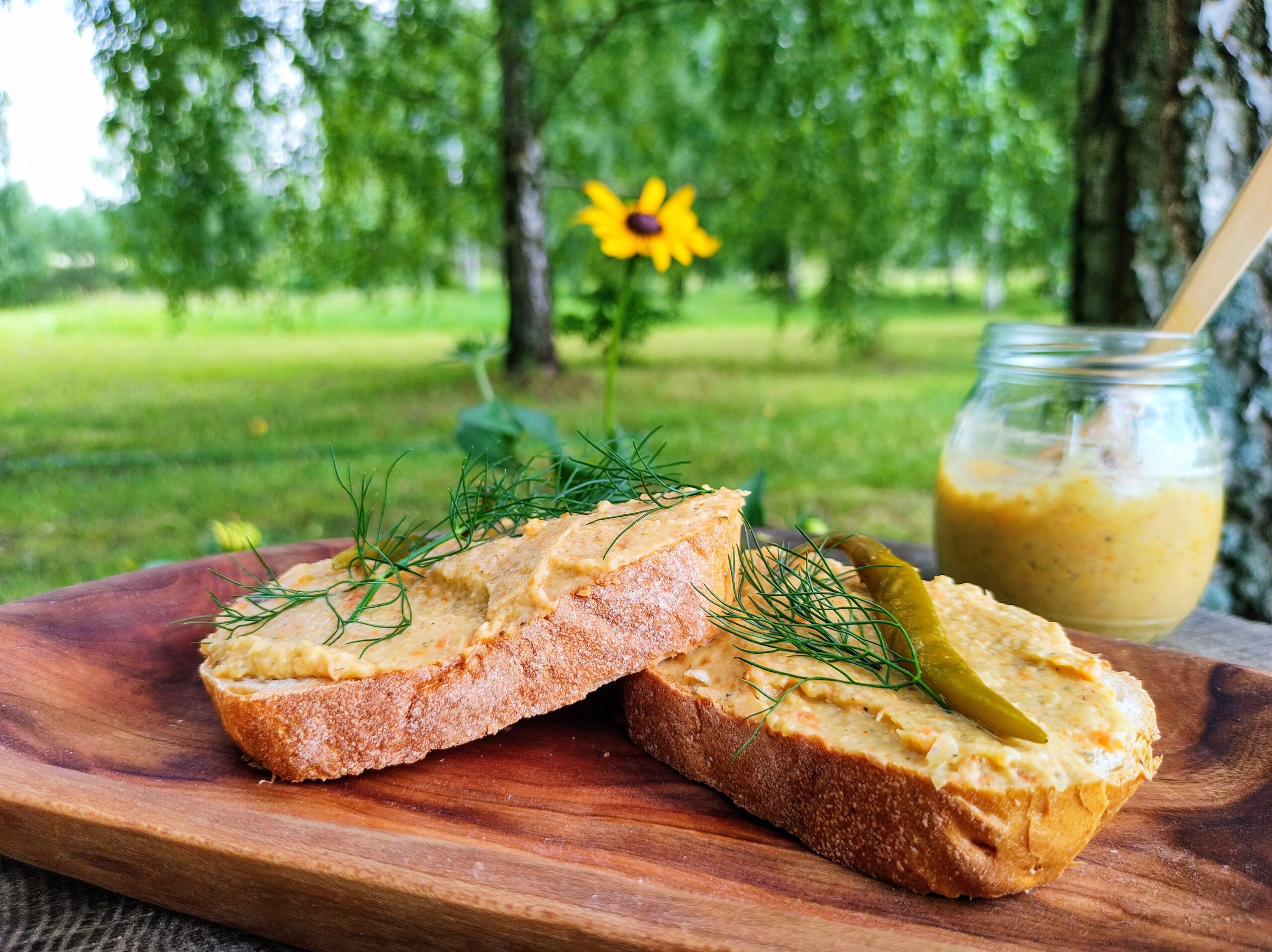 Dwie pajdy chleba z pastą pasztetową podane wśród zieleni.