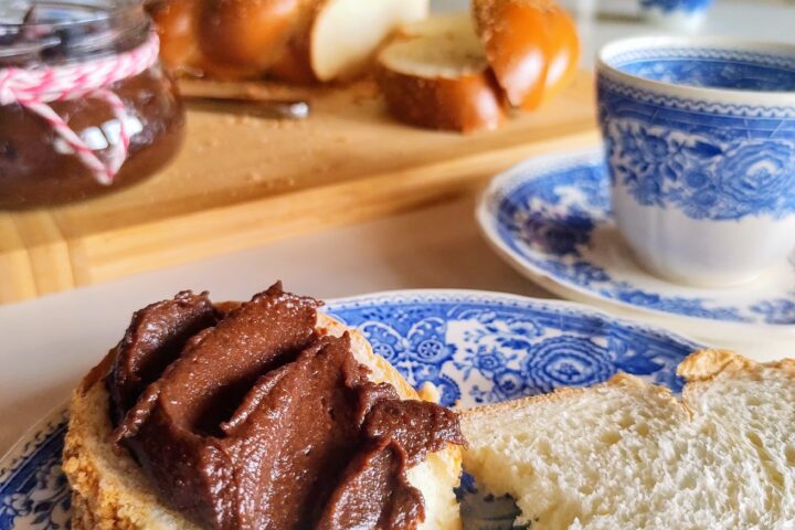 Obrazek przedstawia stół zastawiony do śniadania, na talerzu kromka chałki z kremem czekoladowym.