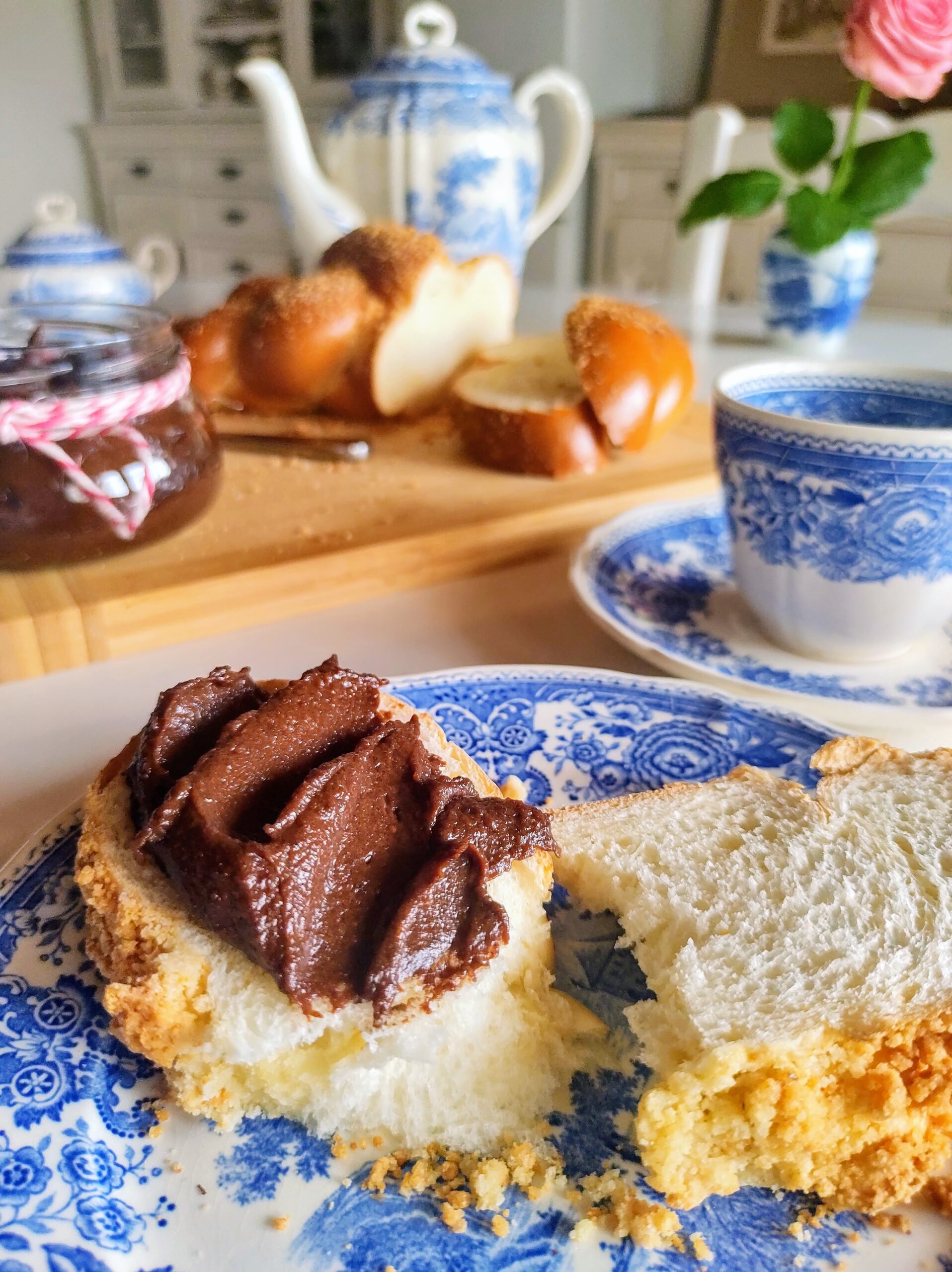 Obrazek przedstawia stół zastawiony do śniadania, na talerzu kromka chałki z kremem czekoladowym.