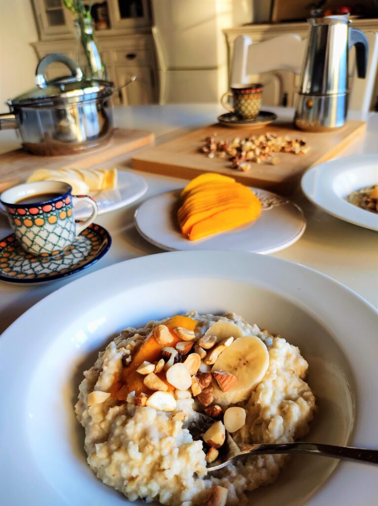 Poranny stół przygotowany do śniadania - w talerzach owsiana jaglanka z mango, bananem i z orzechami.